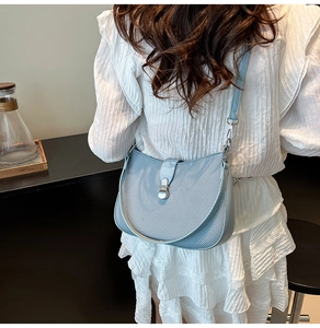 Side view of light blue woven shoulder bag with silver clasp on white lace outfit