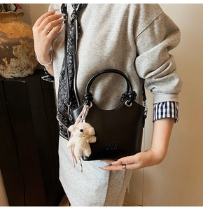 Détail du sac seau noir avec bord ondulé, poignée ronde et breloque ours en peluche