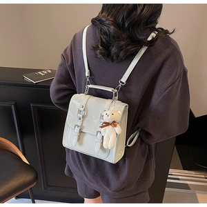 Detail view of light grey shiny PU mini backpack with bear charm and metallic buckle straps