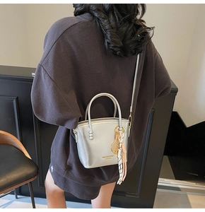 Silver metallic bucket bag with logo print and pink tassel worn across a waffle hoodie