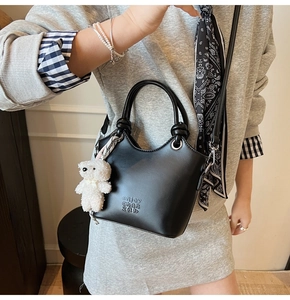 Détail du sac seau noir avec texte embossé, breloque ours et foulard à motifs