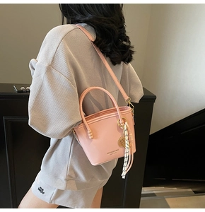 Detail of pink bucket bag with leaf charm and striped scarf on adjustable strap
