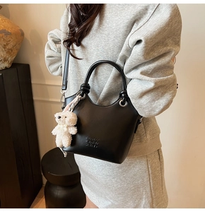 Détail d'un sac seau en cuir noir mat avec poignée et accessoire charm ours en peluche