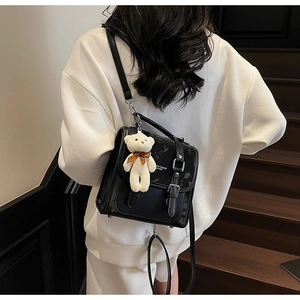 Detail view of black vintage PU backpack with metal buckle and plush bear pendant