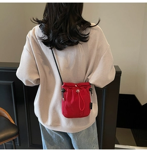 Detail of red drawstring crossbody bucket bag showing fabric texture and compact size
