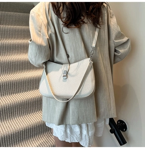 Detail of woven texture and silver lock on ivory crossbody bag worn by a model