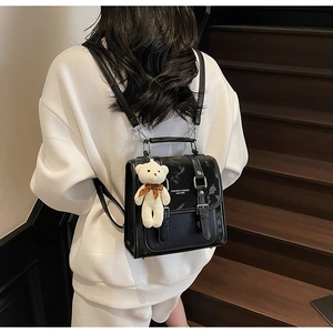 Black leather backpack with flap buckle and white bear pendant on model back