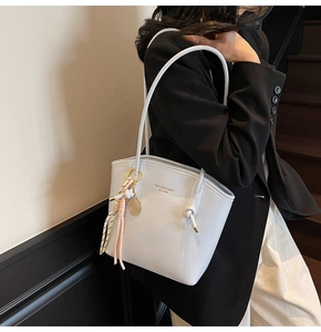 Dettaglio della borsa tote grigio-azzurra con ciondolo da tennis su una modella