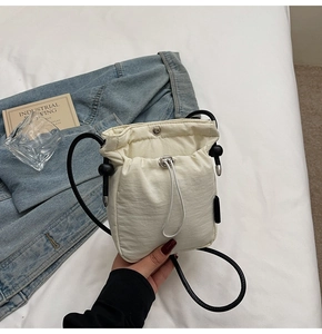 Detail view of a cream mini drawstring bucket bag on a clean white fabric surface