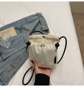 Detail of off-white drawstring crossbody phone bag with black strap and magnetic closure