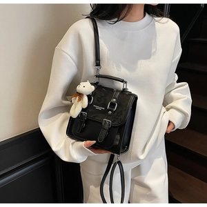 Close-up of black PU leather flap backpack with twin buckles and white plush bear charm
