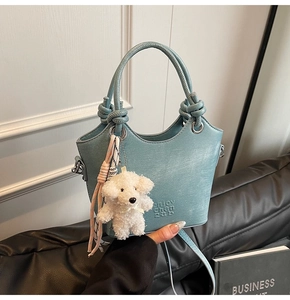 Détail du sac seau bleu clair avec poignée nouée, breloque chien et texte gravé