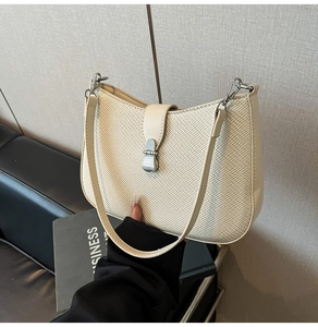 Detail of woven texture and metal clasp on a beige shoulder bag in a lifestyle setting