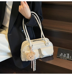 Detail der cremefarbenen Kissentasche mit Vordertaschen und Teddyanhänger auf Holzstufen