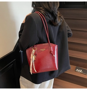 Dettaglio borsa a secchiello in pelle bordeaux lucida con logo dorato e ciondolo in seta chic