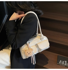Schicke cremefarbene Kissentasche mit Taschen und Bärenanhänger auf schwarzem Blazer