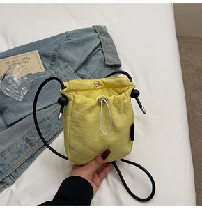 Detail of a bright yellow mini drawstring crossbody bag with black cord straps