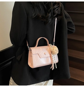 Pink leather crossbody bag with teddy bear charm shown on a black blazer outfit