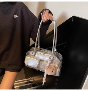 Detail der silbernen Metallic-Schultertasche mit Vordertaschen und Bärenanhänger