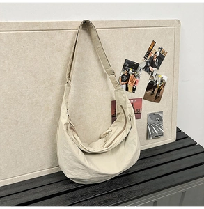 Detail of beige crescent crossbody bag with thick shoulder strap and smooth zipper closure