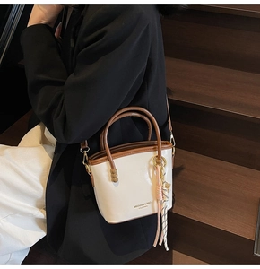 Detail of contrast color bucket bag with braided pendant on dark stairs