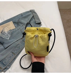 Close-up of bright yellow drawstring crossbody phone bag with textured fabric and metal snap