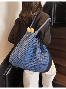 Sac fourre-tout bleu en paille tressée porté par un mannequin sur un escalier en bois chic