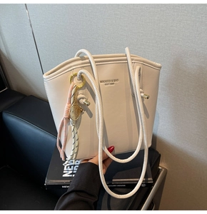 Dettaglio della borsa a secchiello color crema con logo e ciondolo a racchetta
