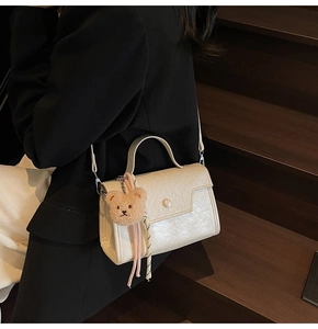 Detail of cream white leather crossbody bag with pearl buckle and cute teddy charm