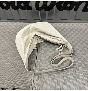 Detailed close-up of beige nylon crescent bag with double zipper and wide strap