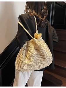 Grand sac fourre-tout en paille tressée crème porté par un mannequin au look décontracté