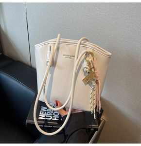 Dettaglio di una borsa a secchiello in ecopelle bianco crema con logo e ciondoli
