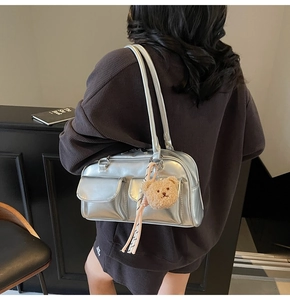 Silberne Metallic-Kissentasche mit zwei Vordertaschen und Bärenanhänger am Modell