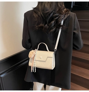 Chic cream-white crossbody bag with cute bear pendant on a model in a black blazer