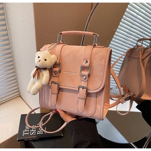 Detailed view of pink glossy backpack with silver buckles and a cute teddy bear charm