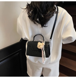 Black cross-body handbag with animal texture and plush bear charm on white hoodie