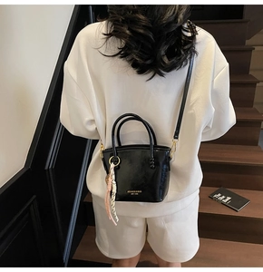 Detail of black glossy crossbody bucket bag with gold lettering and decorative knot charm