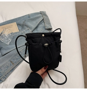 Detail of black crossbody bucket bag with drawstring pocket and metallic snap button