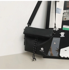 Detail of black crossbody messenger bag featuring decorative drawstring and brand label