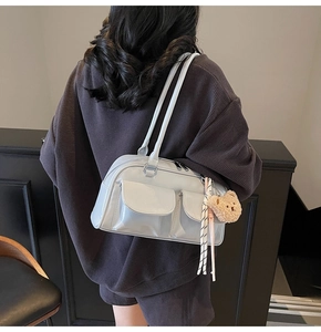 Detail der hellgrauen glänzenden Schultertasche mit zwei Fronttaschen und Bärenanhänger