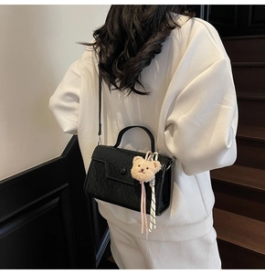 Detail view of black lychee grain crossbody bag with plush bear charm on white sweatshirt
