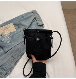 Detail of minimalist black nylon crossbody bag with drawstring closure and silver buckle