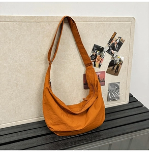 Detail of orange nylon dumpling bag with wide shoulder strap against beige background