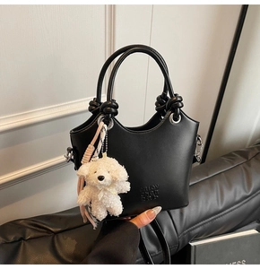 Détail du sac seau en cuir noir avec poignée nouée et porte-clés chien en peluche blanc