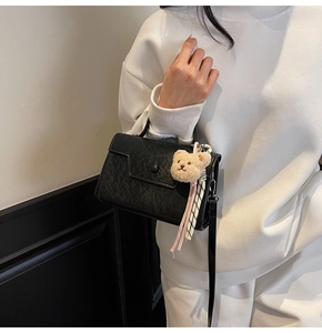 Detail of black crossbody bag with embossed texture, plush bear and ribbon accessory
