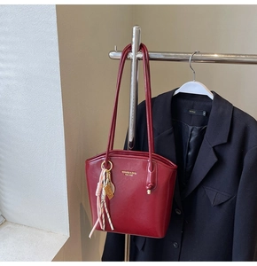 Dettaglio della borsa a secchiello bordeaux lucida con nappa su blazer nero