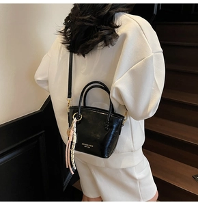 Close-up of shiny black bucket bag with brand logo, metal rings and a woven tassel charm
