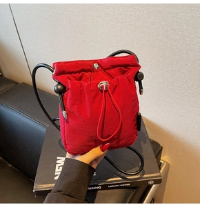 Close-up of a red drawstring bucket bag in wrinkled nylon fabric with black cord strap