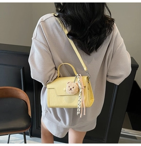 Rear view of a model wearing a light yellow crossbody bag with a plush bear charm