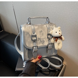 Detail of silver metallic backpack with buckled straps and a white teddy bear charm